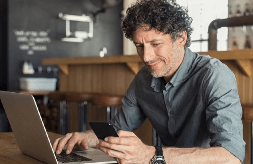 Business owner reviewing business insurance solutions on phone and laptop in a cafe setting