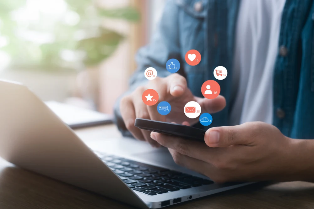 Person using a smartphone and laptop to manage social media and email as part of web marketing services for small businesses.