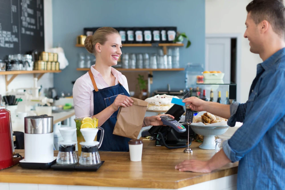 Customer paying at a café counter with a card, illustrating small business checkout with gift card solutions.